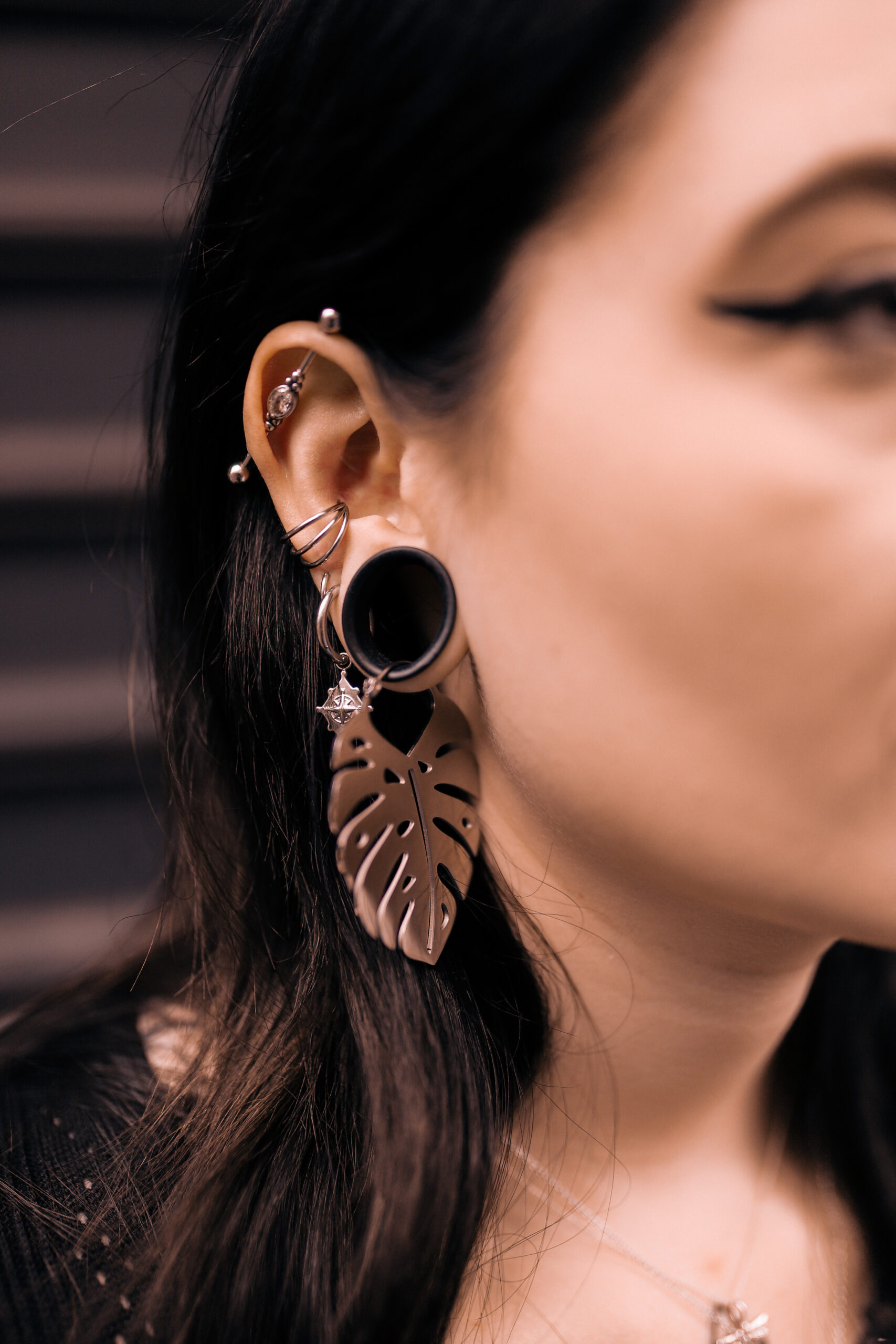 Silberfarbene Monstera-Ohrringe aus Chirurgenstahl, getragen am Ohr einer Frau, vor dunklem Hintergrund