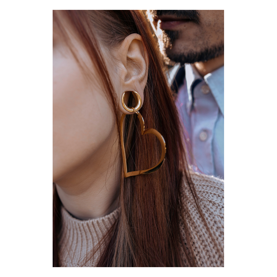 Ruusukultaiset sydänkorvakorut naisen korvassa, taustalla mies