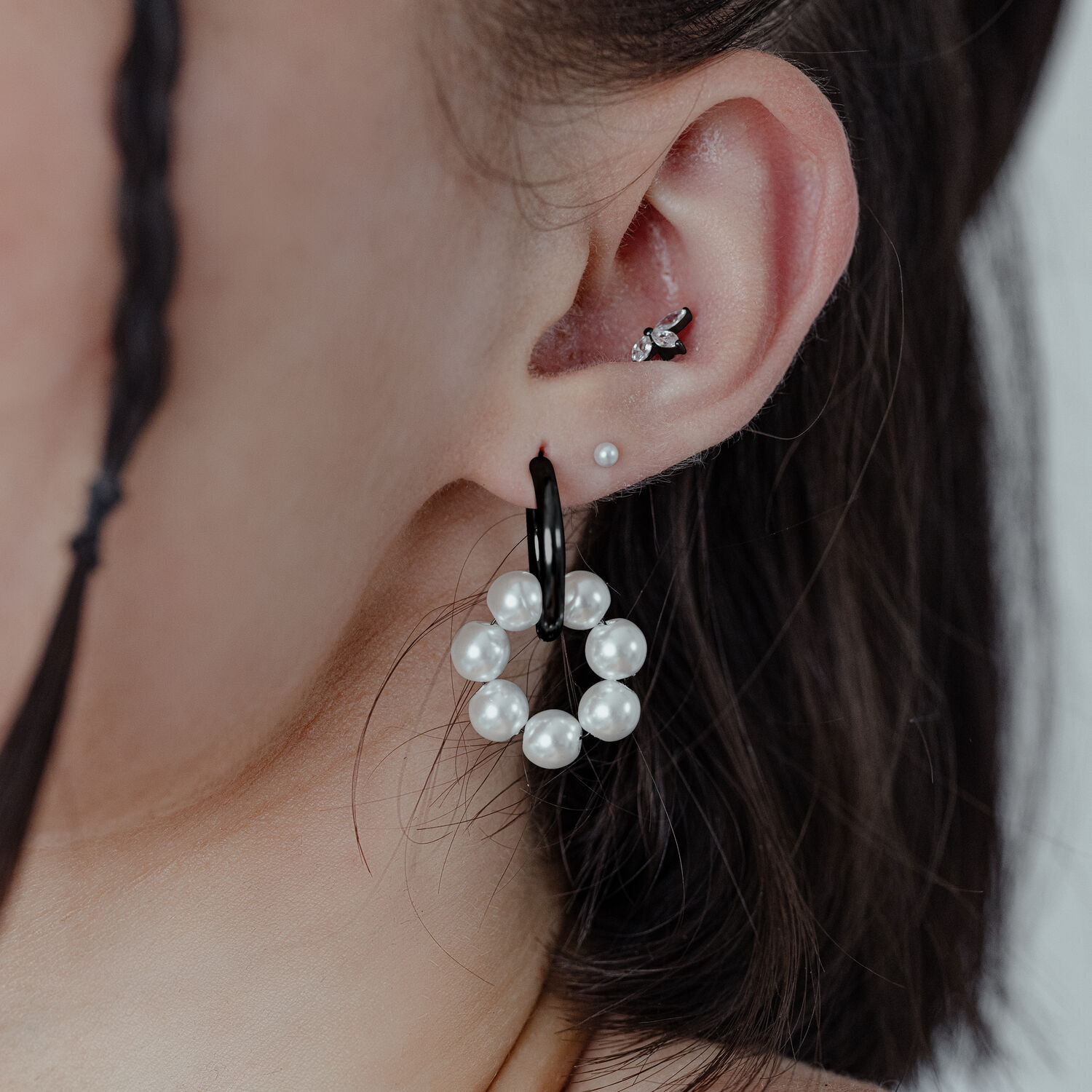 Schwarze Perlen-Ohrringe am Ohr Schwarze Creolen mit kleinen Perlen an einem Ohr, Nahaufnahme