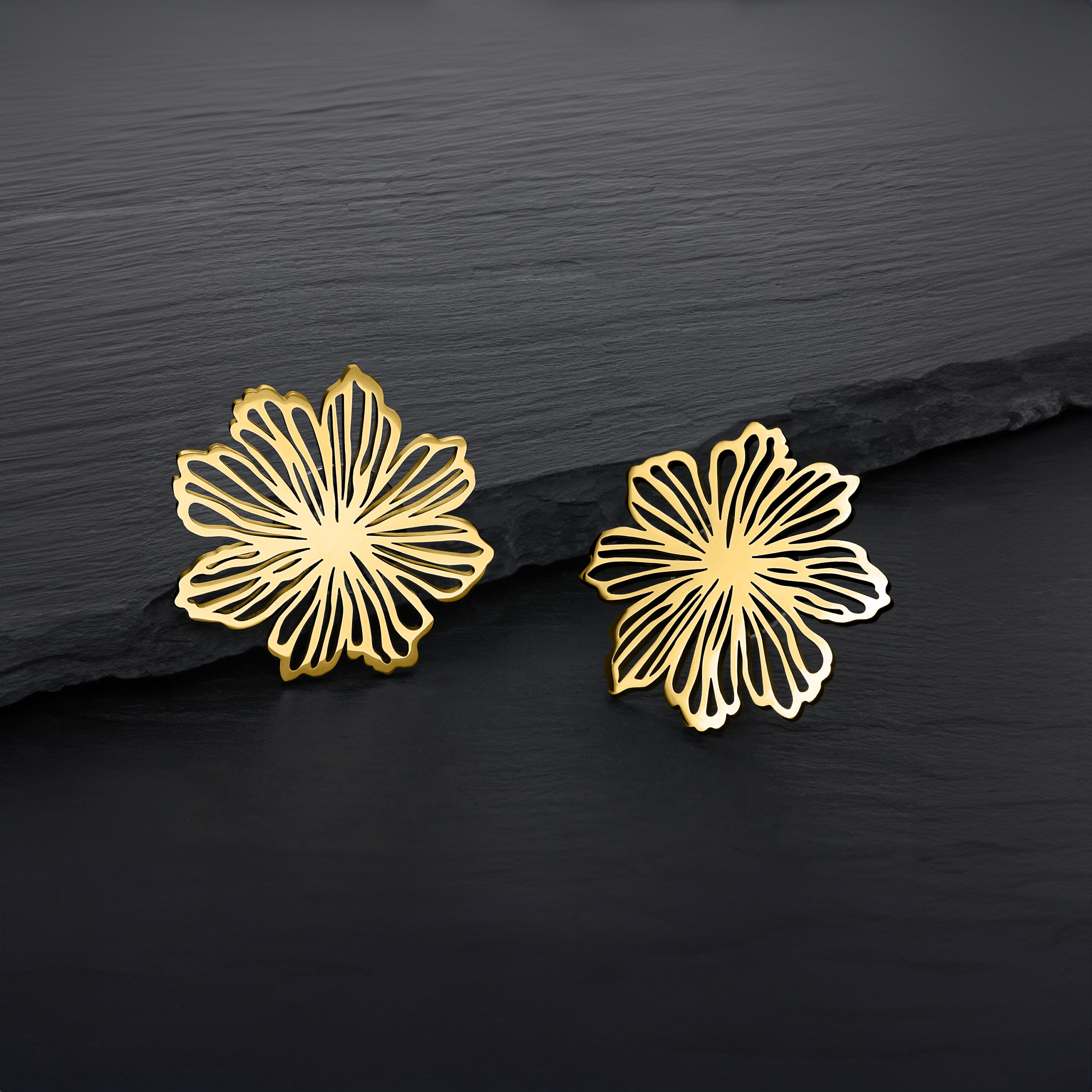 Zwei goldene Blumen Ohrstecker auf dunklem Hintergrund