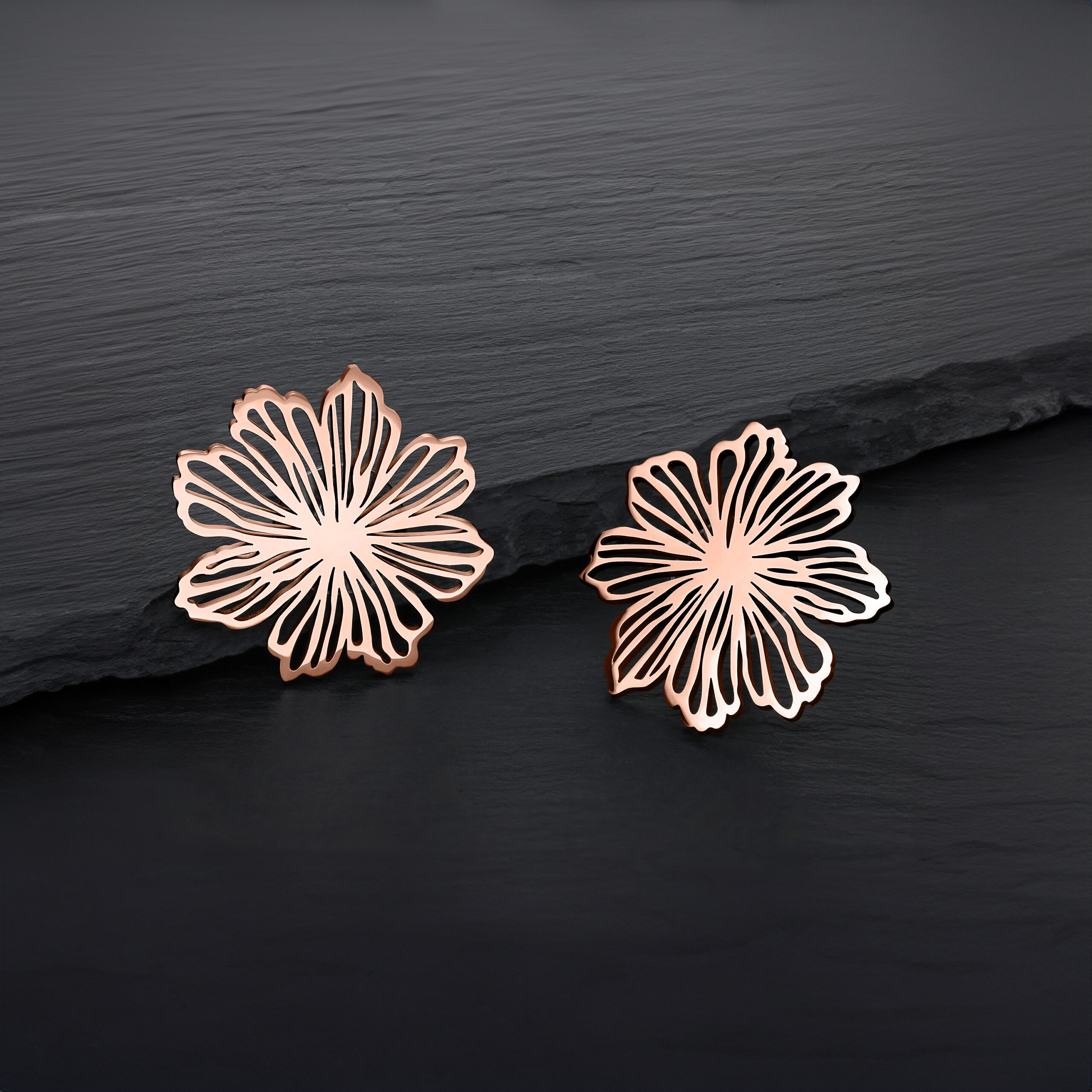 Zwei roségoldene Blumen-Ohrstecker auf schwarzem Hintergrund