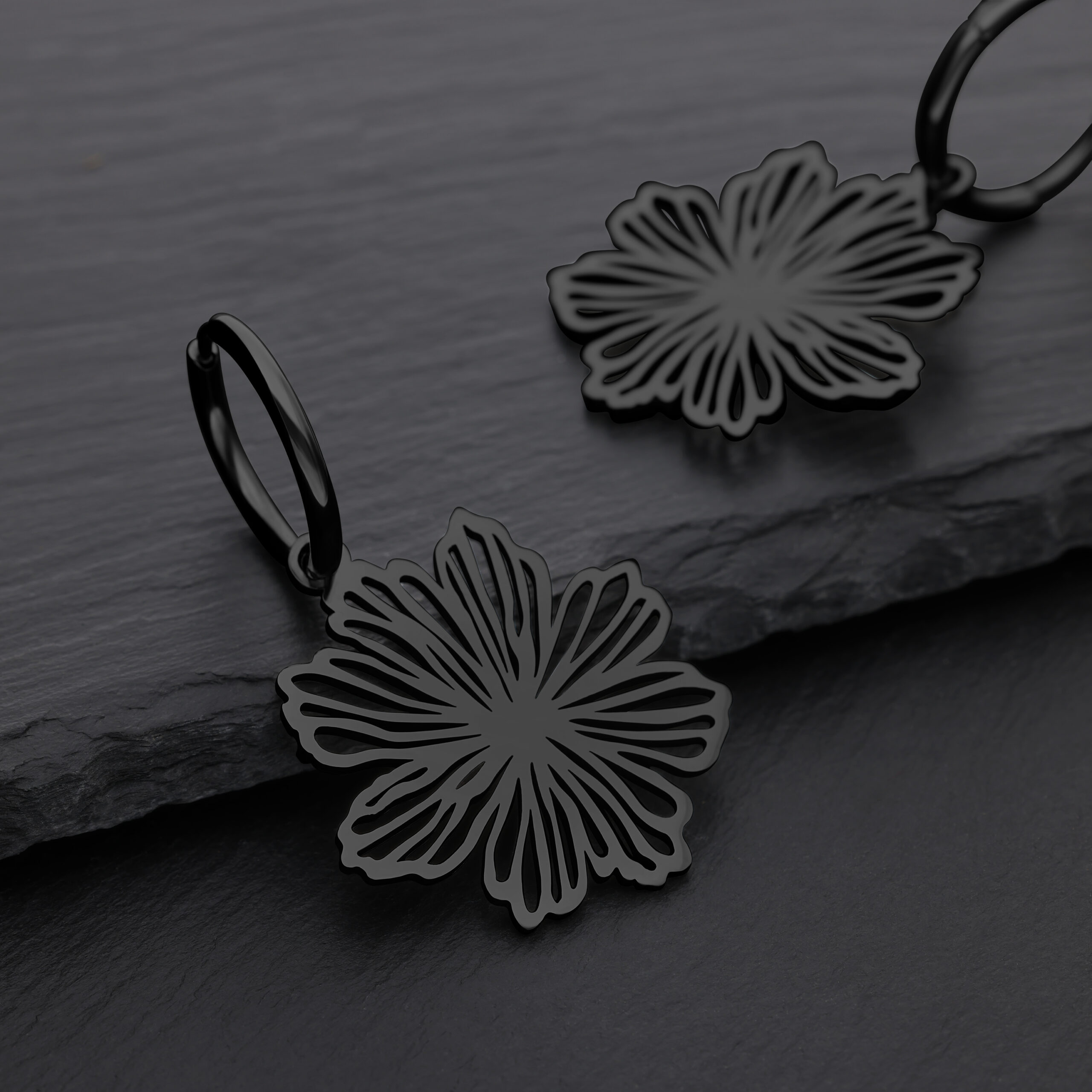 Schwarze Blumenohrringe aus Chirurgenstahl auf grauem Hintergrund