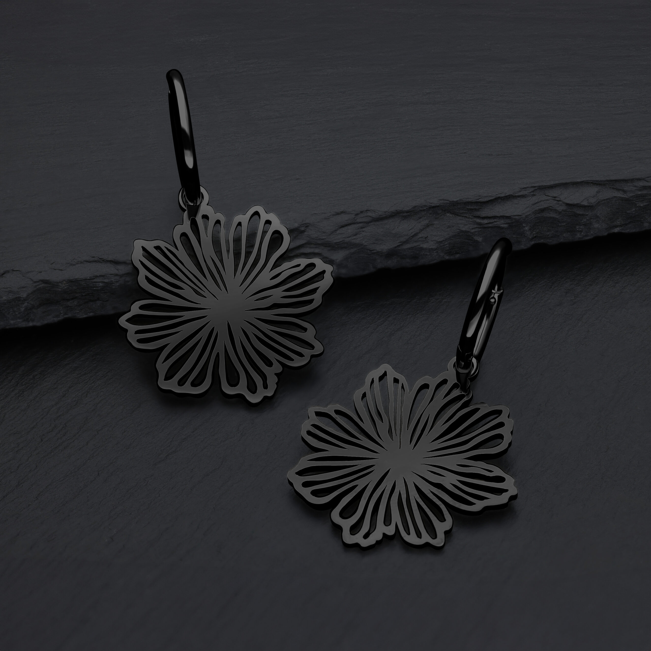 Schwarze Ohrringe in Blumenform aus Chirurgenstahl auf grauem Hintergrund