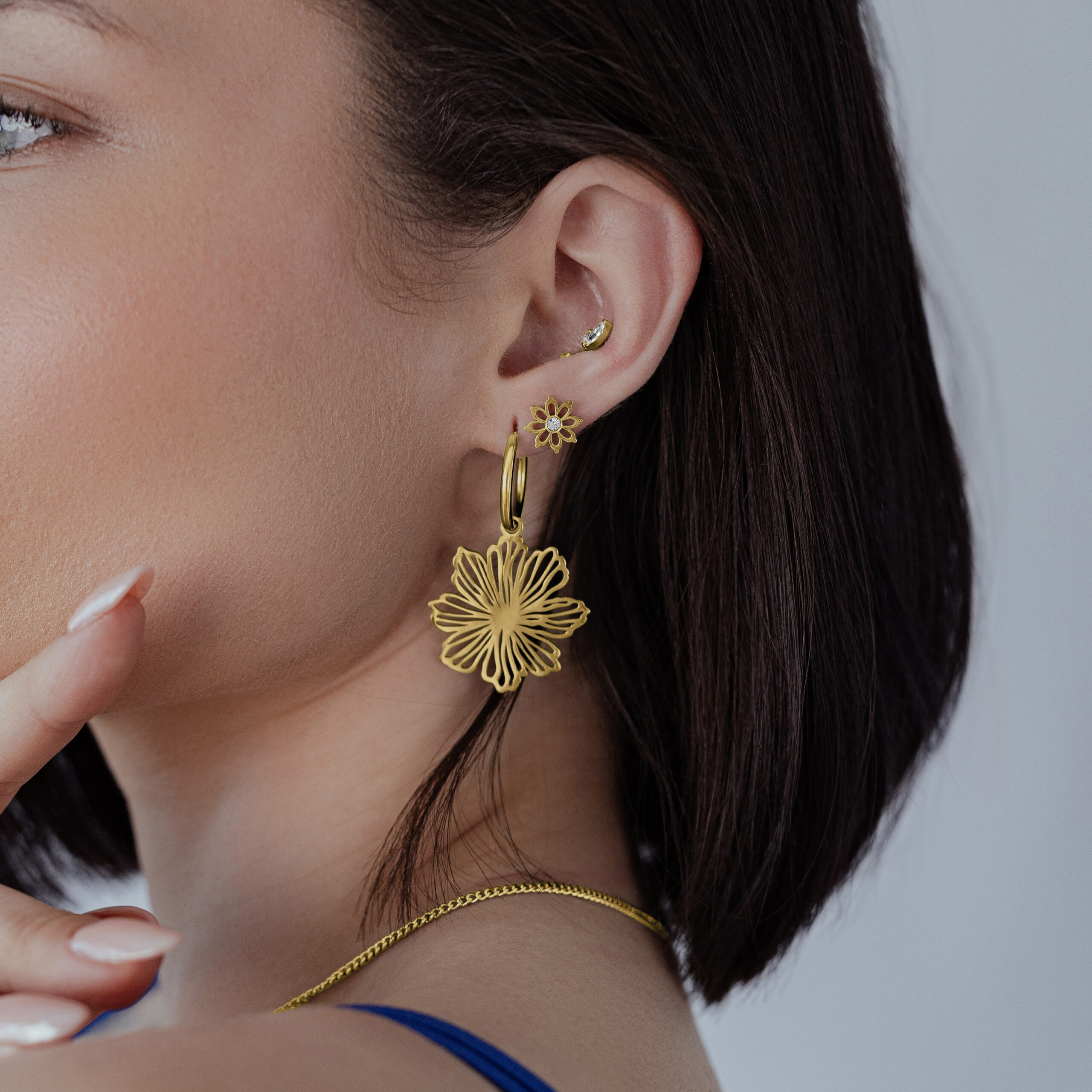 Goldene Fine Flower Hoops Ohrringe Frau trägt goldene Fine Flower Hoops Ohrringe vor neutralem Hintergrund