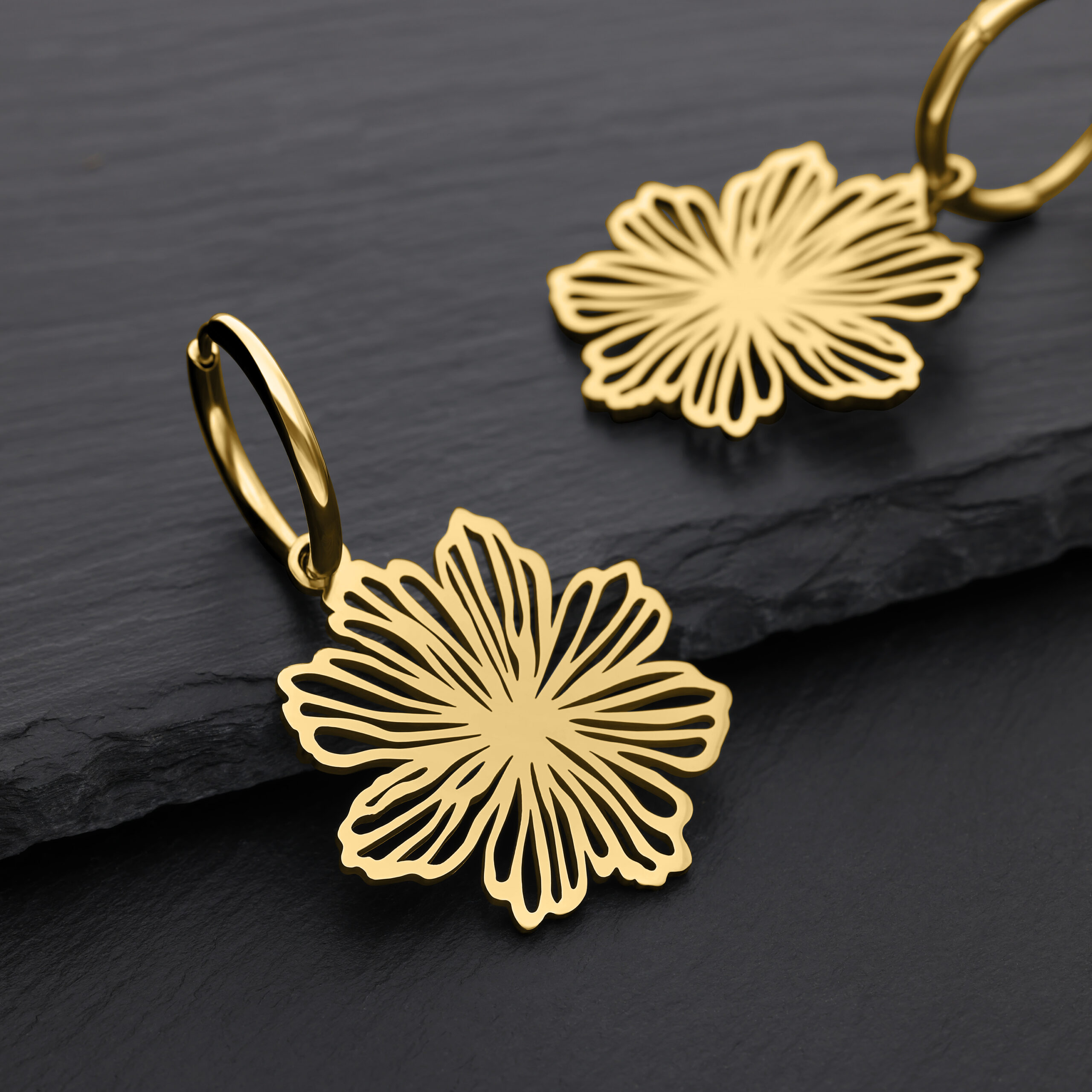 Goldene Fine Flower Hoops aus Chirurgenstahl Zwei goldene Ohrringe in Blütenform auf schwarzem Hintergrund