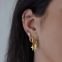 Goldene Hängekreolen mit Kreuzanhänger Goldene Ohrringe mit Kreuzanhänger an einem Ohr, seitliche Ansicht