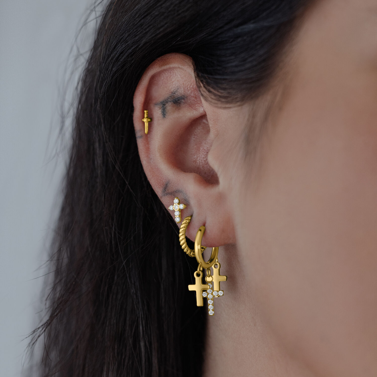 Goldene Hängekreolen mit Kreuzanhänger Goldene Ohrringe mit Kreuzanhänger an einem Ohr, seitliche Ansicht