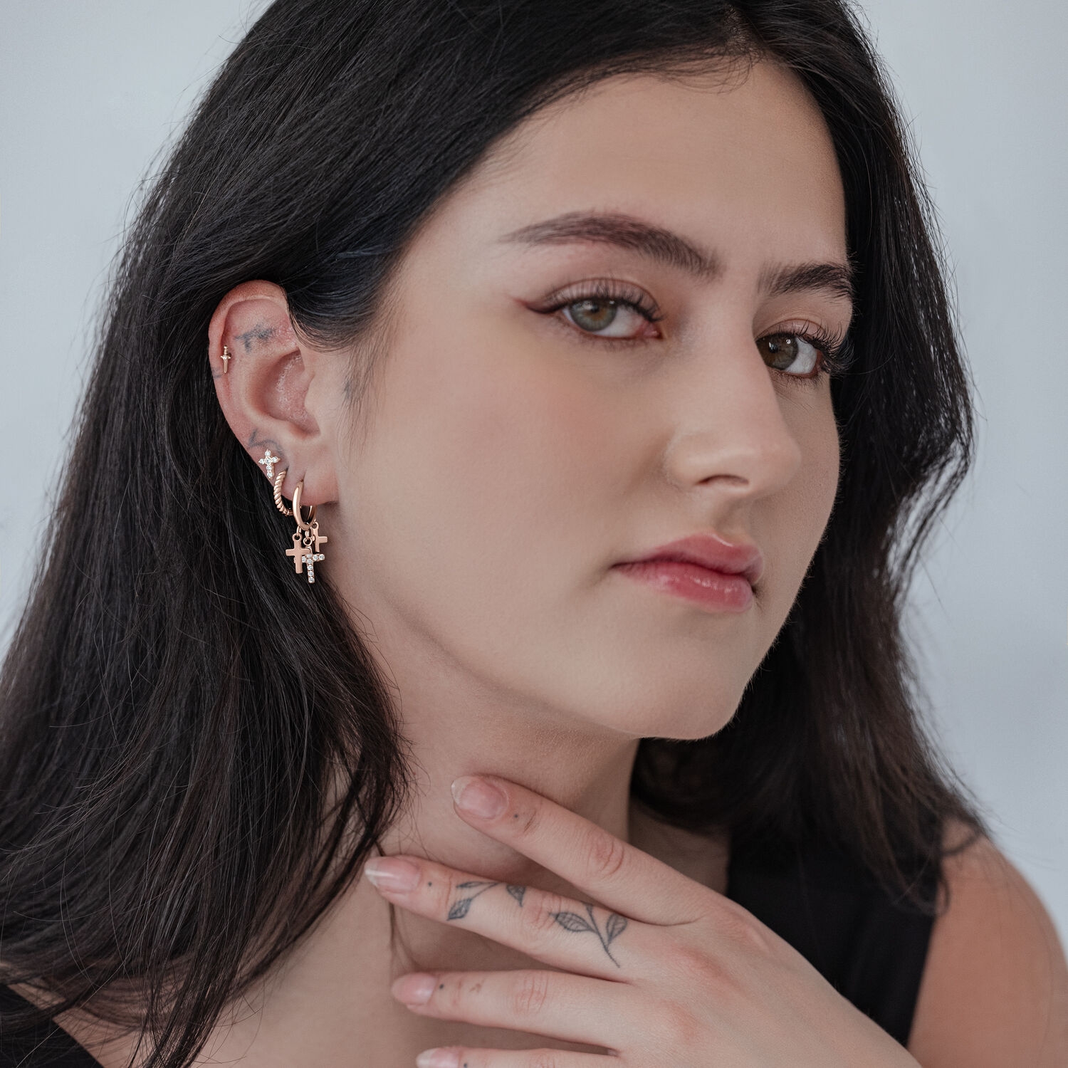 Nainen ruusukultaisilla pienillä ristikorvakoruilla neutraalilla taustalla