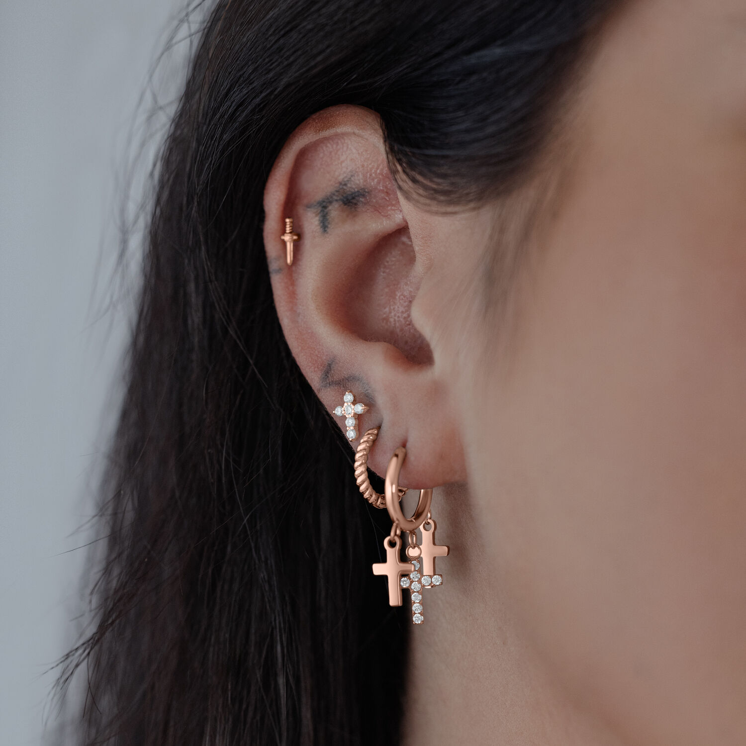 Lähikuva ruusuhopeisista renkaista, joissa pienet ristiriipukset korvassa.