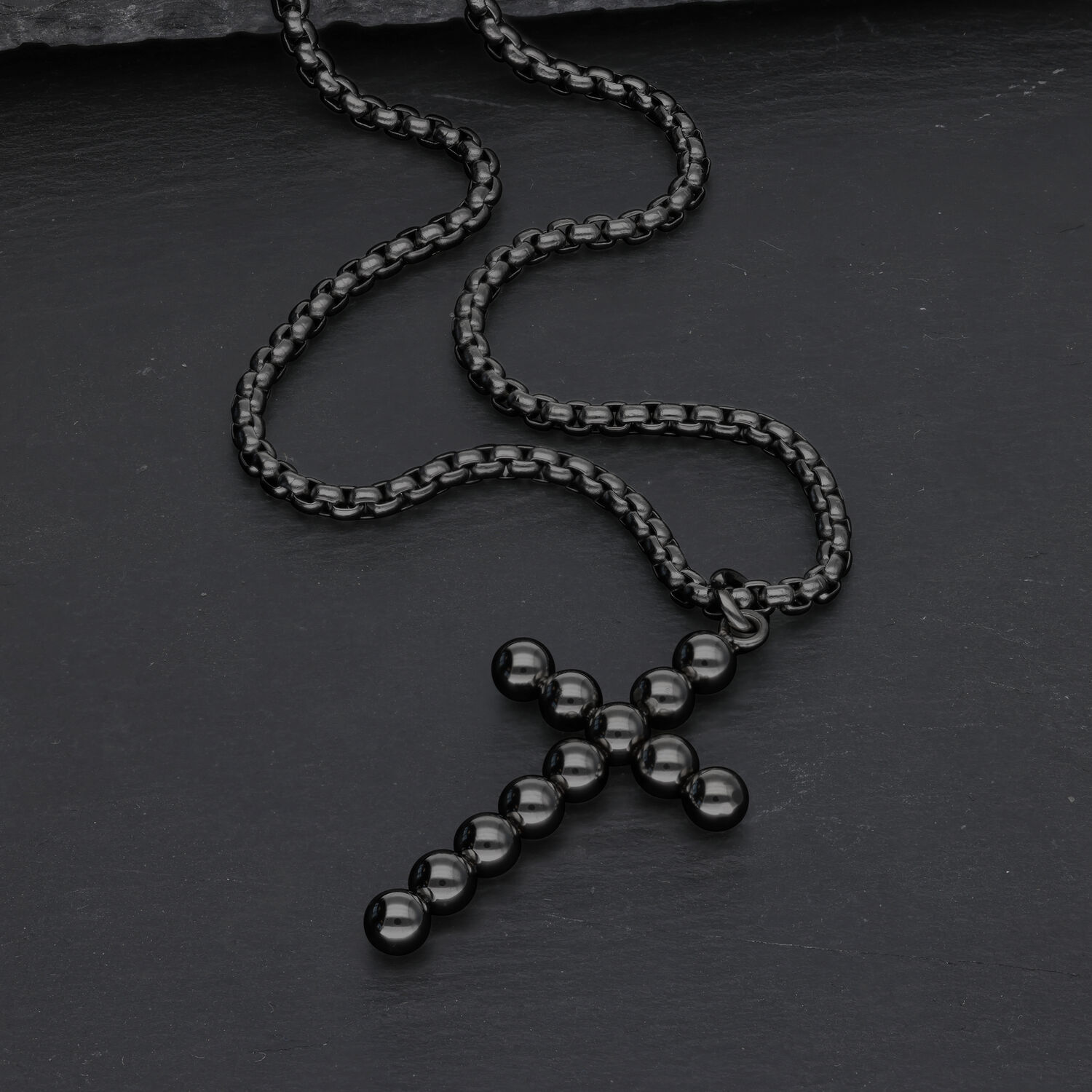 Schwarze Halskette mit Kreuzanhänger aus Kugeln auf dunklem Hintergrund