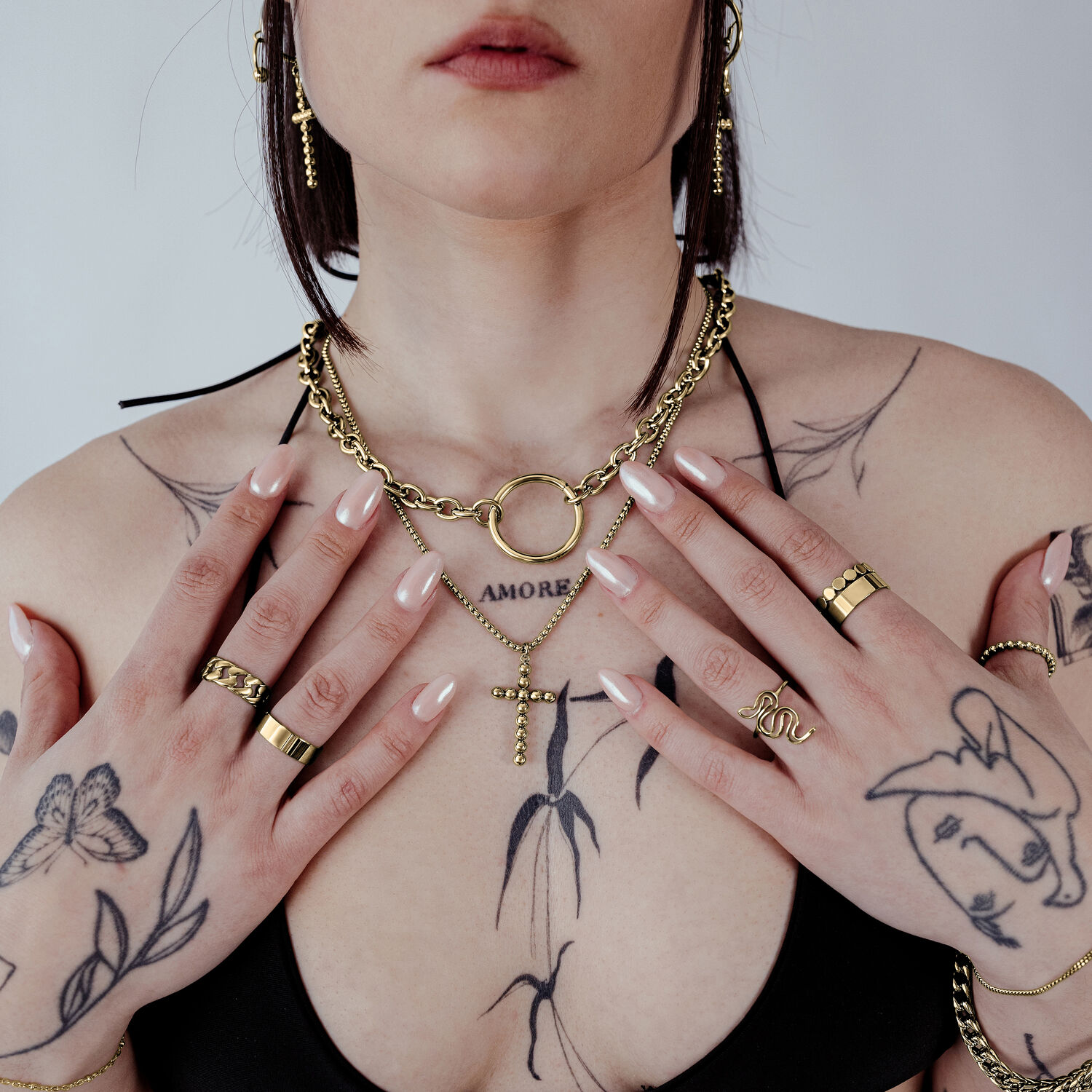 Frau mit goldener Bubble Cross Halskette und Tattoos auf hellem Hintergrund