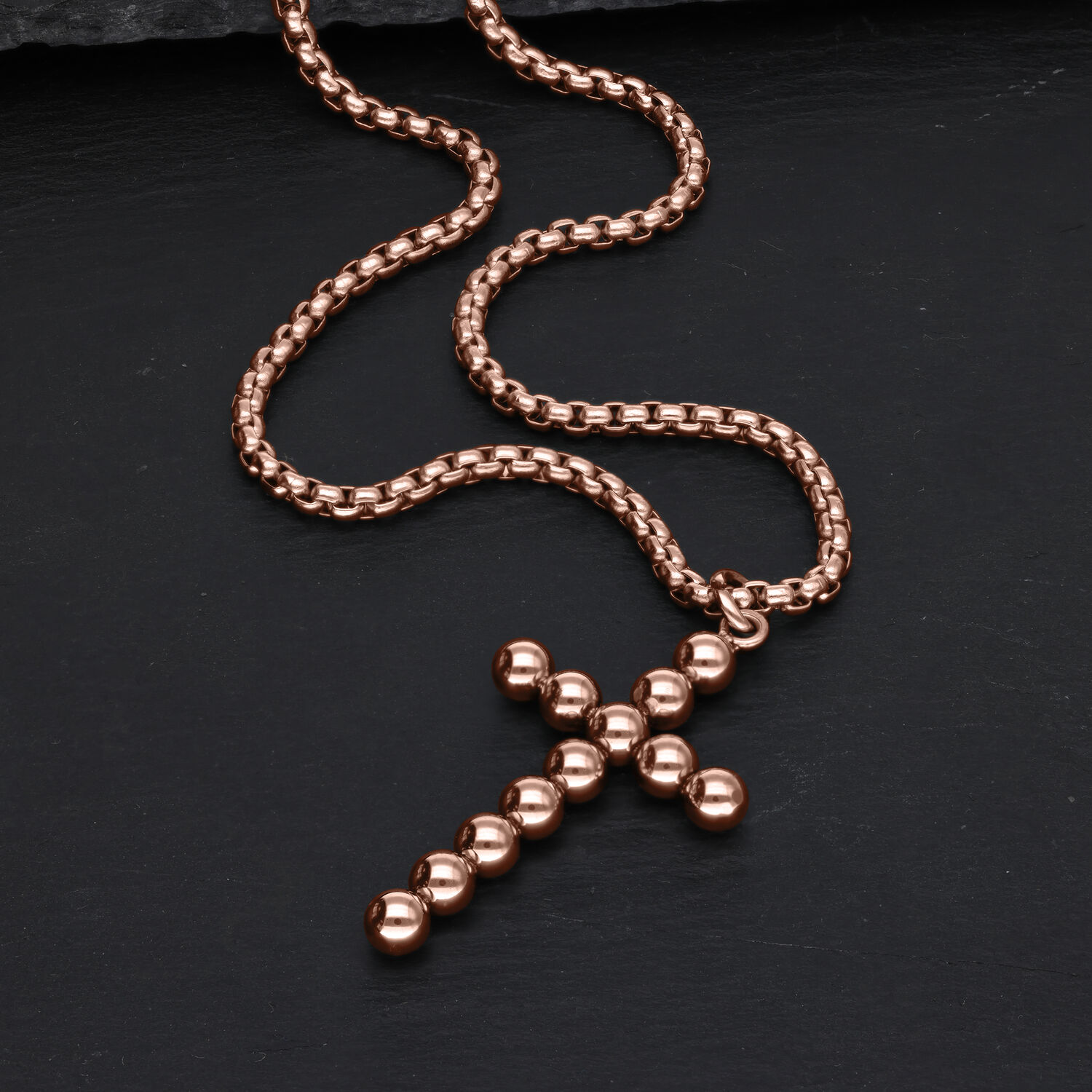 Ruusukultainen kaulakoru, jossa on ristiriipus pallokuvioilla mustalla taustalla