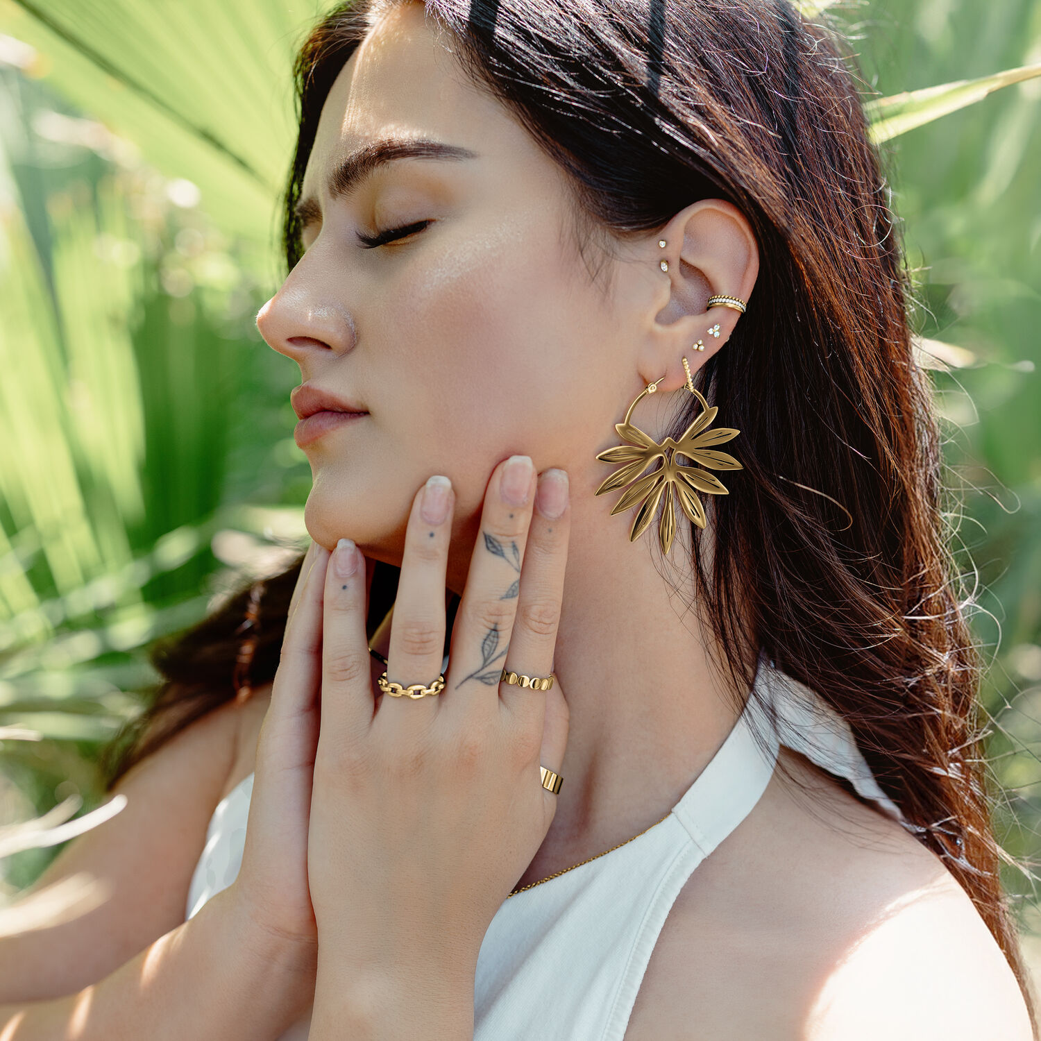 Frau mit goldenen Bambus-Ohrringen vor grünen Blättern, entspannter Sommerstil