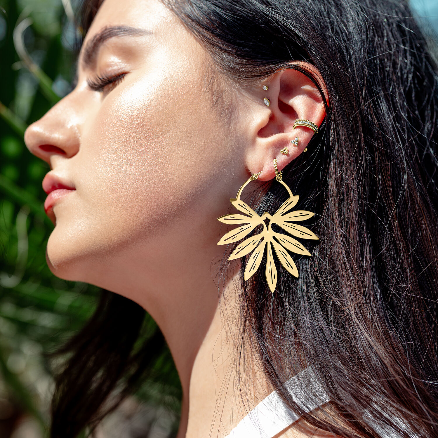 Frau mit goldenen Bambus-Ohrringen vor unscharfem, grünem Hintergrund