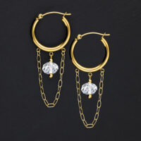 Goldene Metallohrringe mit weißen Steinen und Ketten auf schwarzem Hintergrund