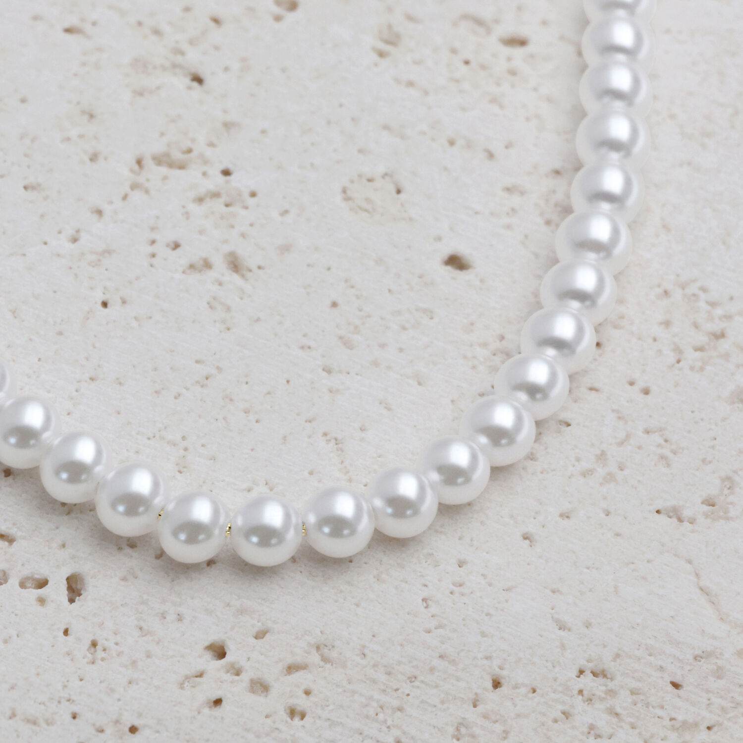 Große synthetische Perlenkette mit goldenen Metallelementen auf hellem Hintergrund