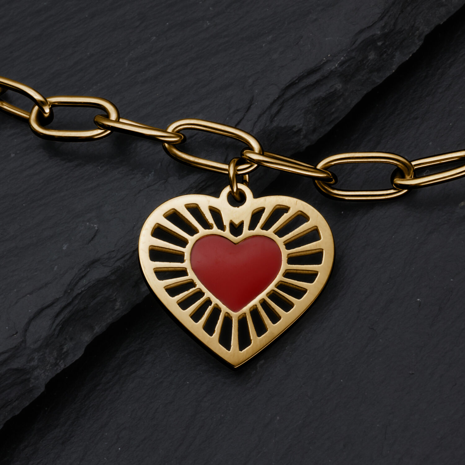 Goldenes Sacred Heart Armband mit rotem Herz Armband aus goldfarbenem Metall mit herzförmigem Anhänger und rotem Herz auf Schieferhintergrund