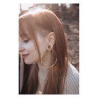 Pitkähiuksinen nainen käyttää suuria ruusukultaisia onttoja korvarenkaita