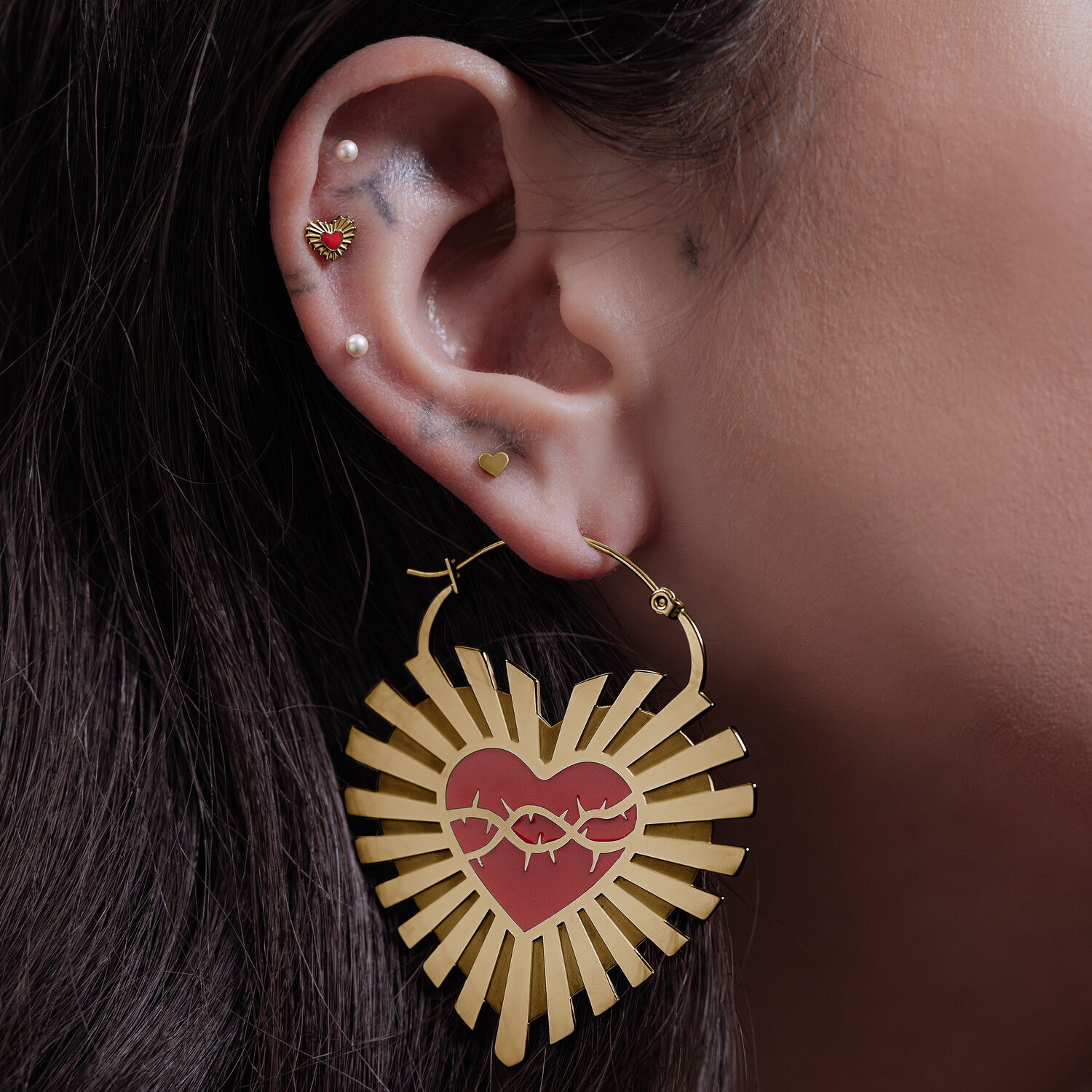 Goldene Sacred Heart Creolen - Wildcat Goldene Barbed Wire Sacred Heart Creolen am Ohr einer Frau vor neutralem Hintergrund