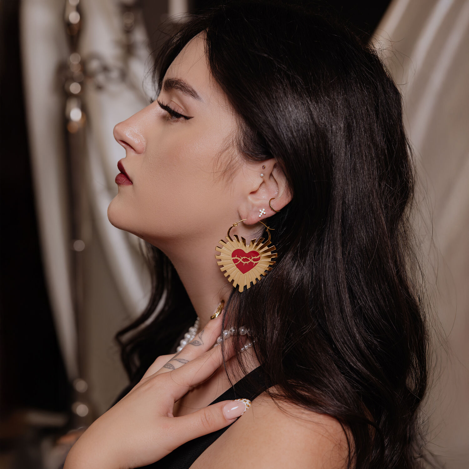 Goldene Herz-Ohrringe mit Stacheldraht-Design Goldene Herz-Ohrringe mit Stacheldraht in Ohr einer Frau mit dunklem Haar