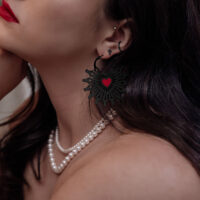 Schwarze Sacred Heart Hoops Ohrringe Frau trägt schwarze Sacred Heart Hoops Ohrringe mit rotem Herzdetail, Nahaufnahme