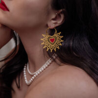 Goldene Sacred Heart Creolen Ohrringe Goldene Creolen Ohrringe mit rotem Herz auf einer Frau