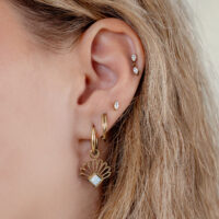 Goldene Opal-Fan Creolen am Ohr Goldene Creolen mit synthetischem Opal an weiblichem Ohr, blondes Haar