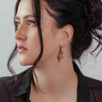 Frau mit goldenen Glamour Hoops Ohrringen vor neutralem Hintergrund