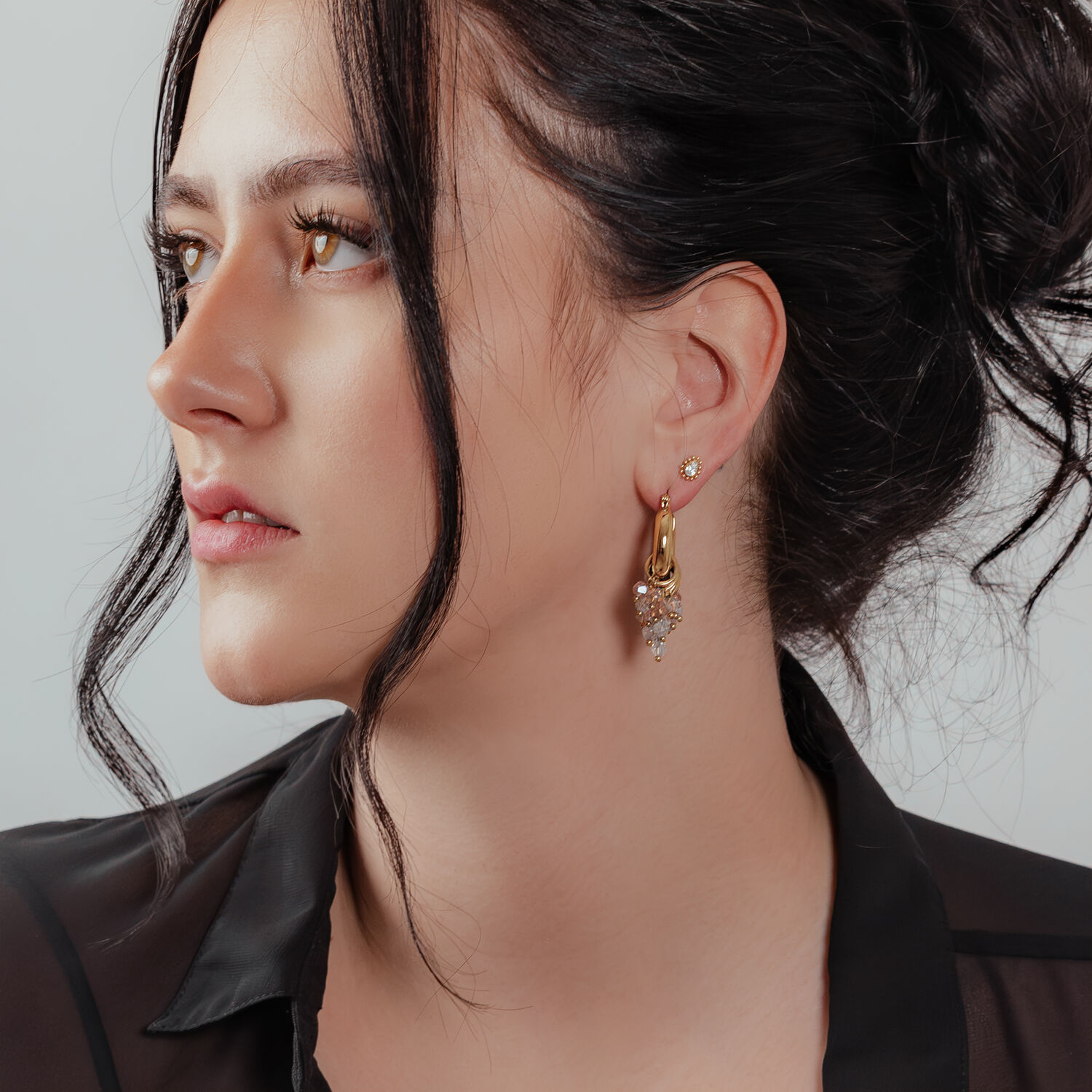 Frau mit goldenen Glamour Hoops Ohrringen vor neutralem Hintergrund