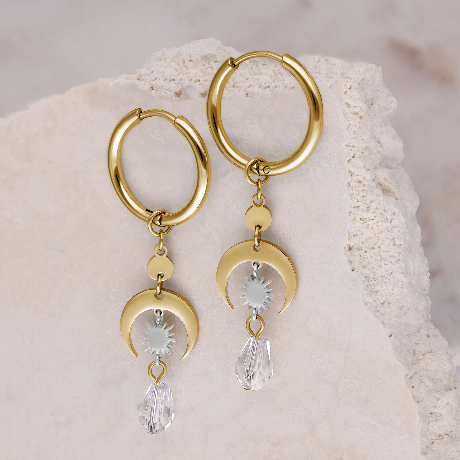 Zwei goldene Creolen auf hellem Stein, mit klarem Kristallanhänger