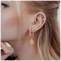 Goldene Clover Hoops Ohrringe am Ohr einer Frau, auf hellem Hintergrund