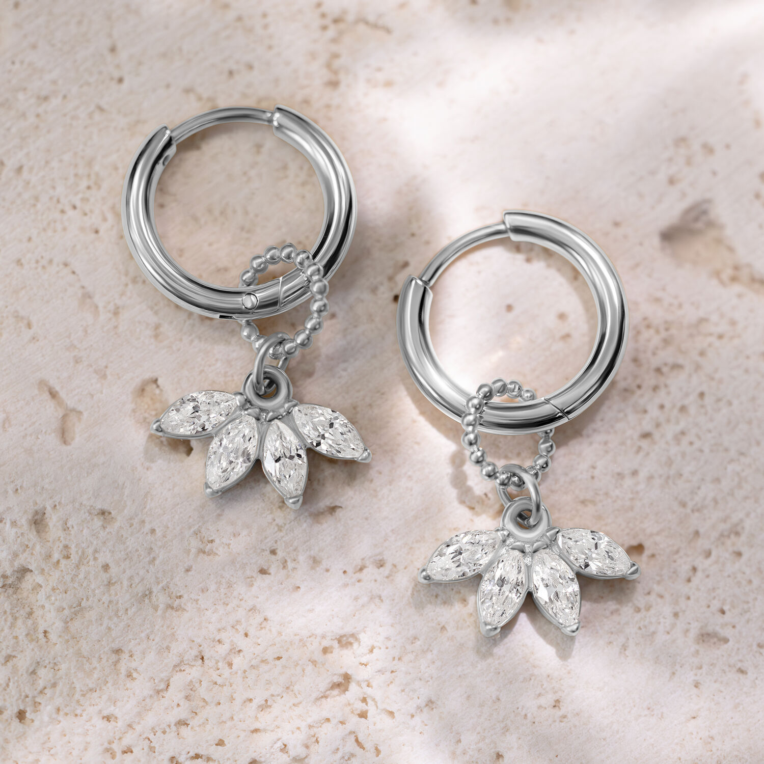 Kaksi hopeista korvakorua kristallinkirkkailla riipuksilla vaalealla kivellä