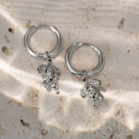 Kaksi hopeista korvarengasta pienillä kilpikonna-riipuksilla vaalealla kivialustalla