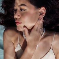 Nainen hopeisilla korvakoruilla ja helmiketjulla, sivulta valaistuna