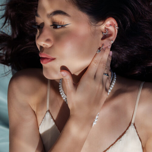 Nainen hopeisilla korvakoruilla ja helmiketjulla, sivulta valaistuna