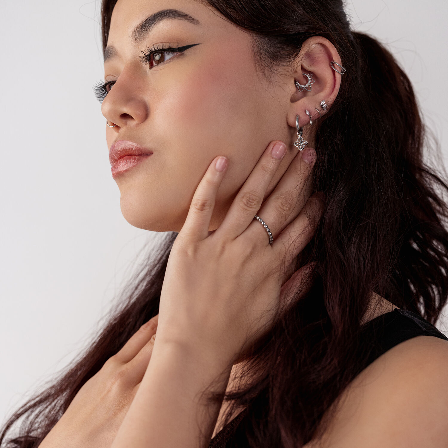 Nainen, jolla on useita hopeisia kukkakuvioisia korvakoruja, sivuprofiili