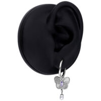 Hopeinen korvakoru, jossa lila perhosriipus ja helmi mustassa korvamallissa