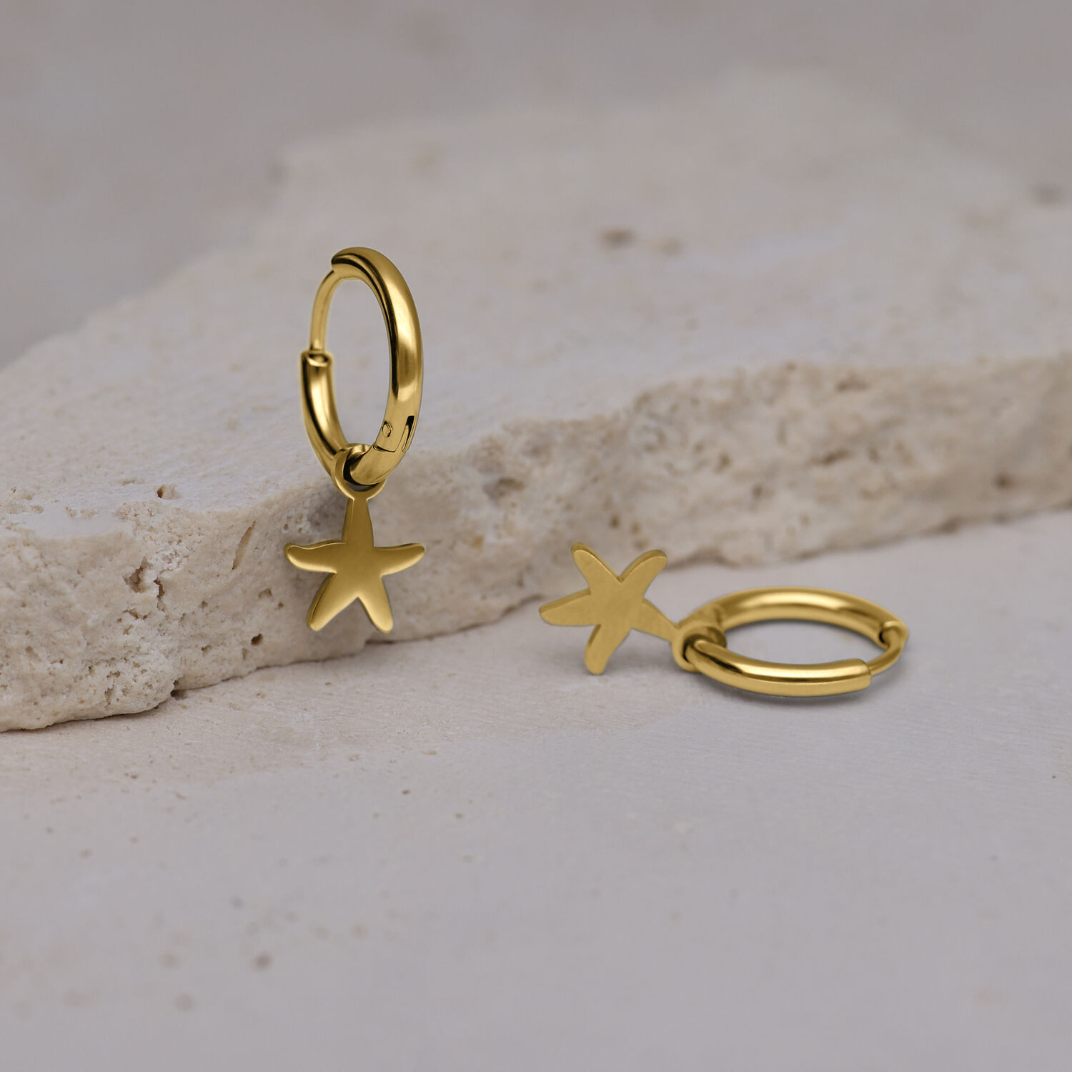 Kaksi kultaista korvarengasta meritähden muotoisilla riipuksilla kivipinnalla