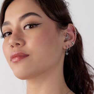 Nainen, jolla on useita hopeisia korvakoruja, mukaan lukien mini meritähti kreolit, valkoista taustaa vasten