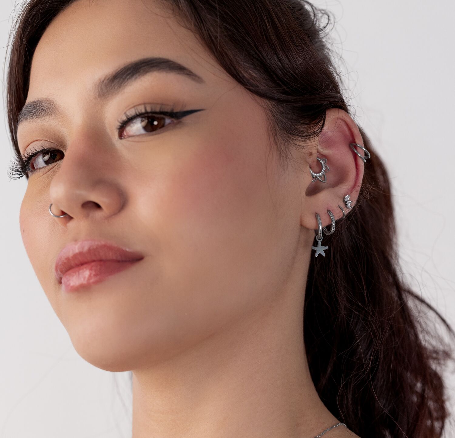 Nainen, jolla on useita hopeisia korvakoruja, mukaan lukien mini meritähti kreolit, valkoista taustaa vasten