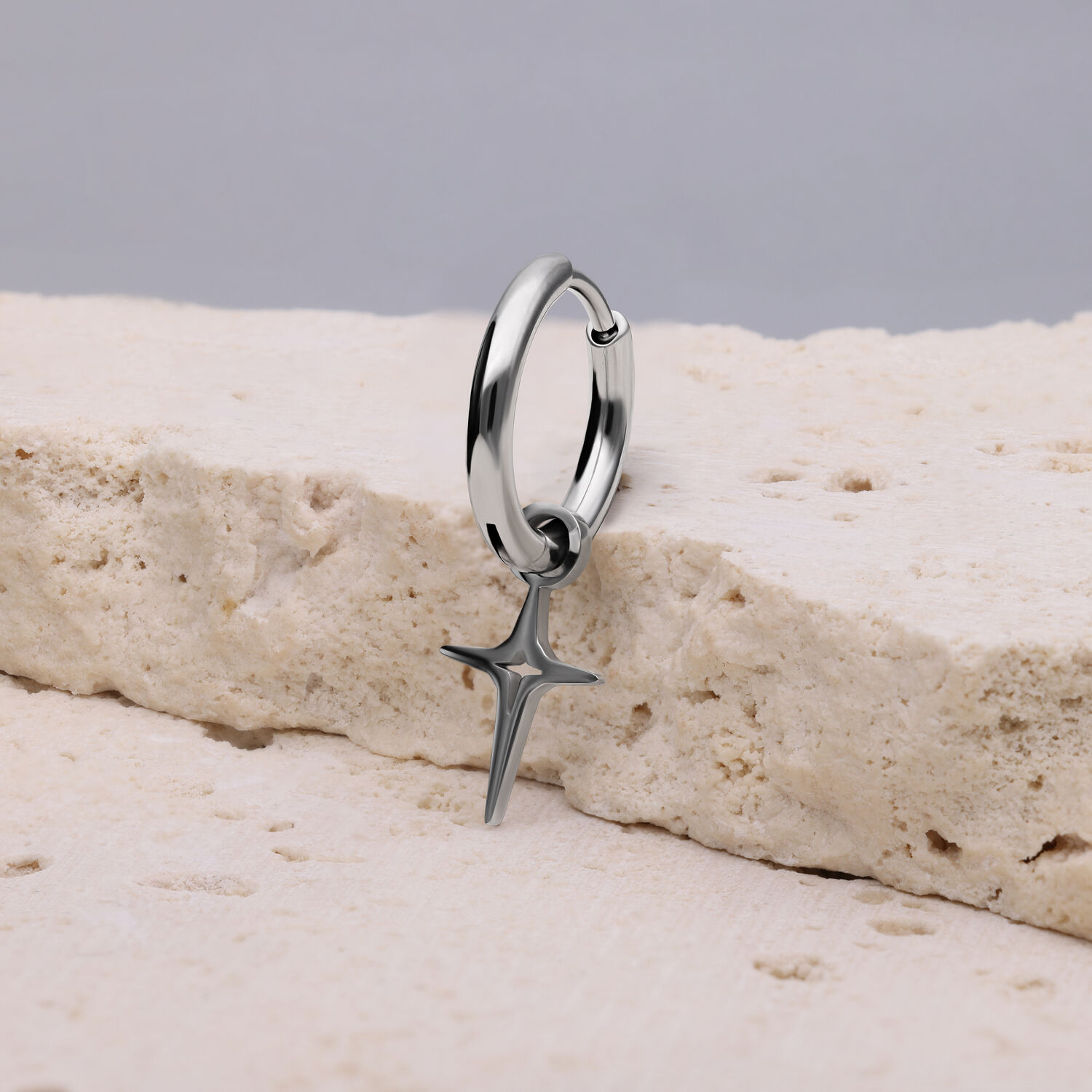 Hopeinen korvakoru, jossa on polaritähtimuotoinen riipus vaalealla kivellä