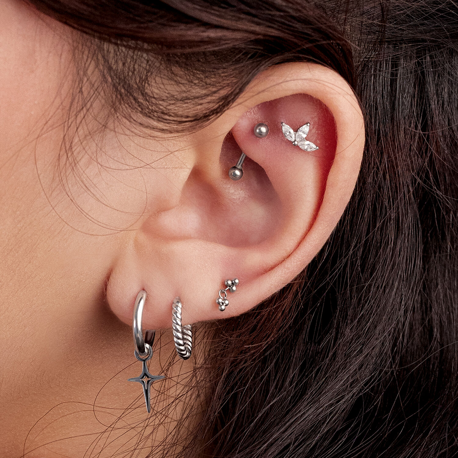 Lähikuva korvasta, jossa on useita hopeisia korvakoruja, mukaan lukien Mini-Polar Star -pari.