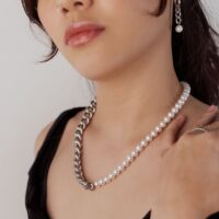 Nainen hopea- ja helmikoristeisella kaulakorulla vaalealla taustalla