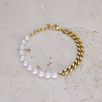 Rannekoru valkoisilla synteettisillä helmillä ja kultaisella lenkkiketjulla beigellä taustalla
