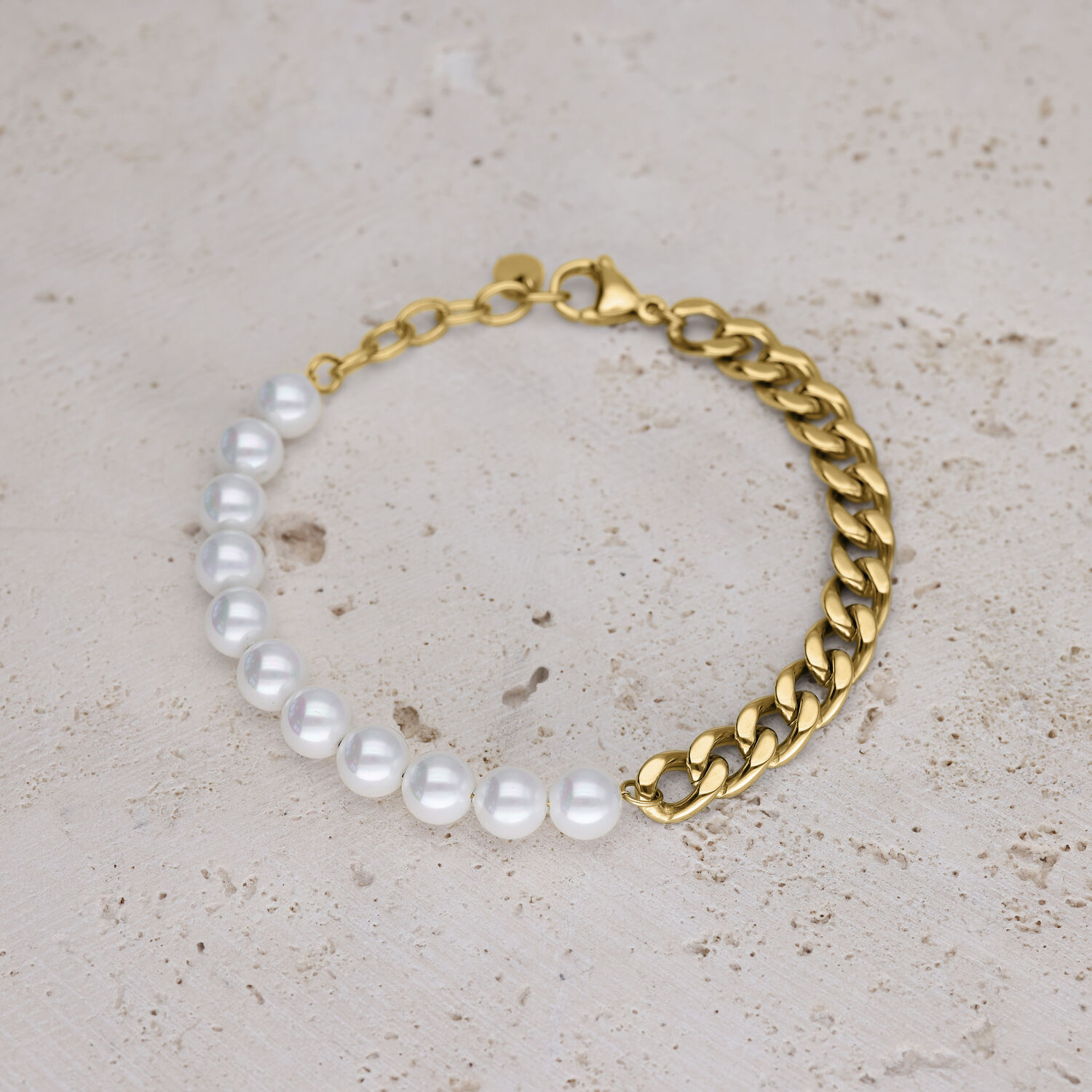 Rannekoru valkoisilla synteettisillä helmillä ja kultaisella lenkkiketjulla beigellä taustalla