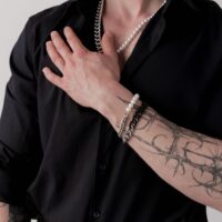 Henkilö mustassa paidassa, jolla on hopeinen ja helmenvalkoinen rannekoru ranteessa