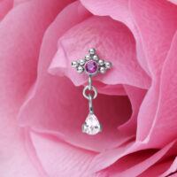 Hopeinen lävistyskoru punaisella kristallilla ja pisaranmuotoinen riipus vaaleanpunaisen terälehden edessä