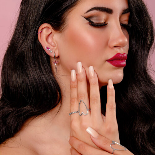 Nainen hopeakorvakoruilla ja punaisella kristallilla vaaleanpunaisella taustalla