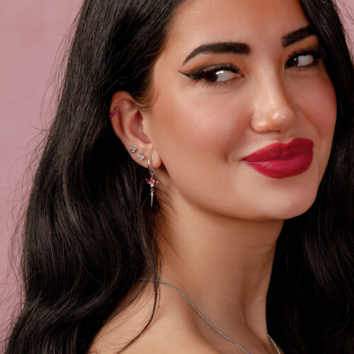 Nainen, jolla on pitkät mustat hiukset ja hopeinen korvakoru punaisella rubiinilla vaaleanpunaisella taustalla