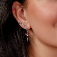 Lähikuva korvasta, jossa on useita hopeisia korvakoruja ja punaisia kristalleja, taustalla tummat hiukset